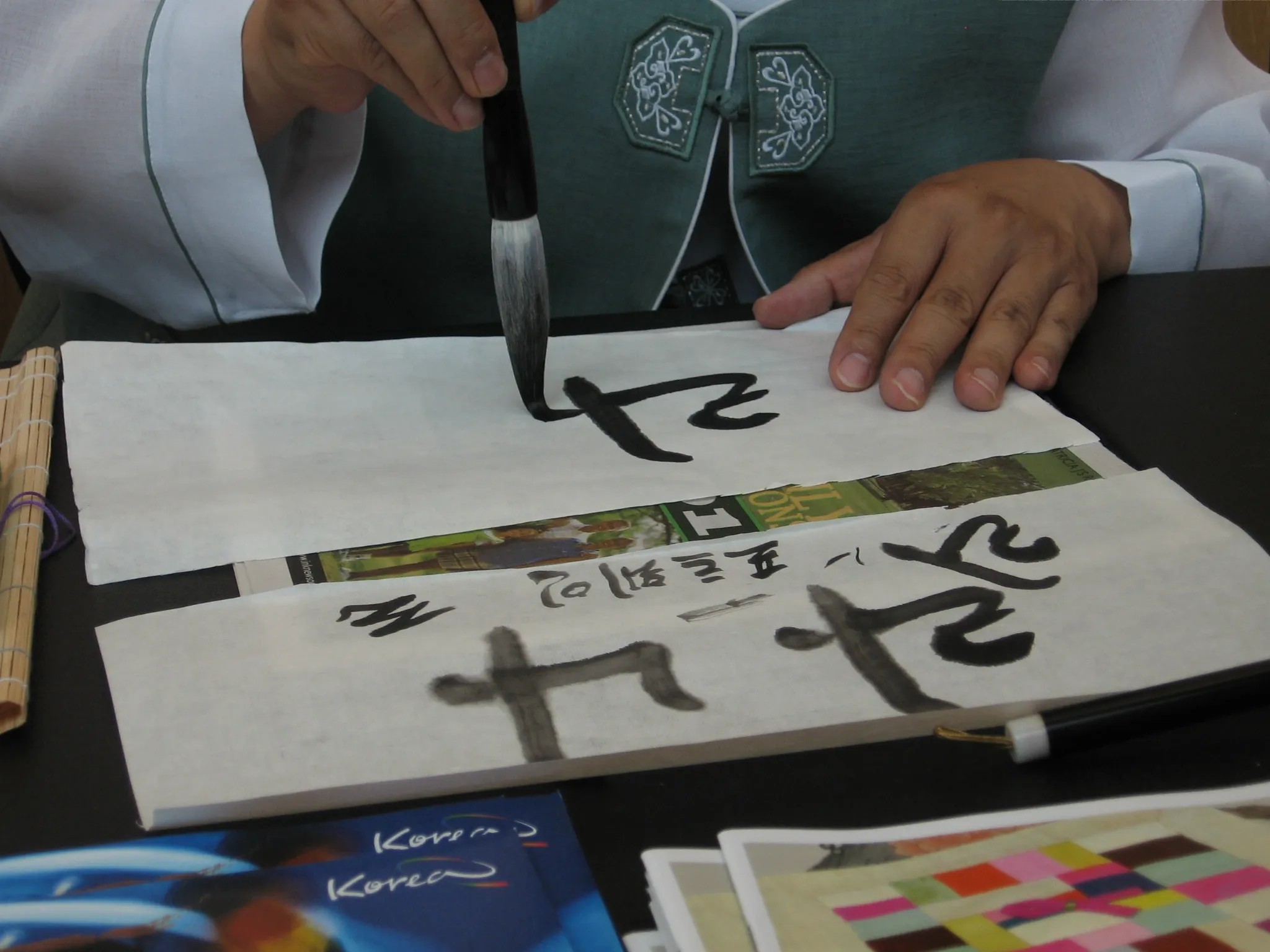 A calligrapher writing Korean hangul characters with a brush on paper